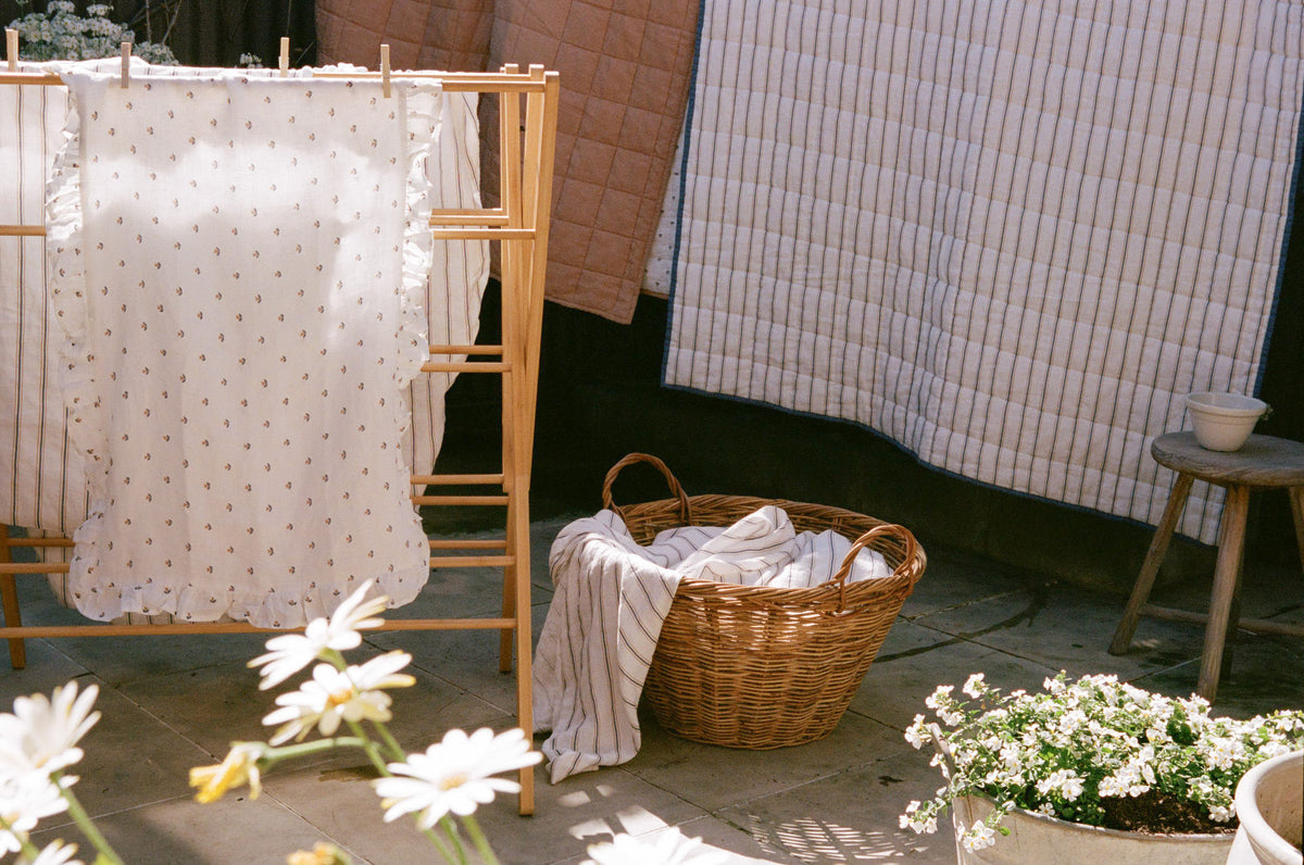 Matilda and Finley linen drying on a washing line and clothes horse, with a washing basket and daisies